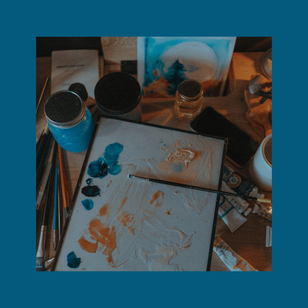 Picture of painting supplies (water jar colored by paint, canvas with various blue paint marks, lots of paint brushes) framed by blue 2026